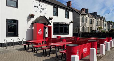 Exterior of Whitecliff Inn with red tables and chairs for seating area.