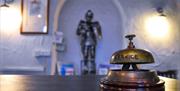 A service bell on a table in front of a suit of armour.