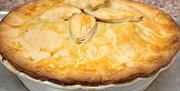 Large home made pie in a white dish with crusty topping and leaf decoration