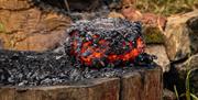 A still glowing red hot lump of iron bloom sits on top of a burnt log