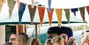 A small crowd gathers around a buffet table for lunch under a parasol with bunting