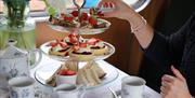 White afternoon tea stand with sanwiches and scones plus cups of tea on white tablecloth