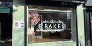 Exterior of Bake bakery in Larne painted light green with black canopy and word BAKE in large window