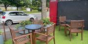 Outdoor eating area with wooden seats, tables, artificial grass and flowers