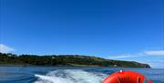 View of Blackhead path and Lighthouse with wake of sea behind boat and life ring visible on Charter NI Boat