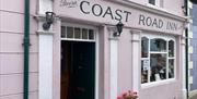 Pink exterior of Coast Road Inn in Glenarm with flowers outside and collectible window display