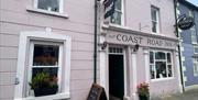 Pink exterior of Coast Road Inn, Glenarm with collectibles window display, flowers and outside chalk board