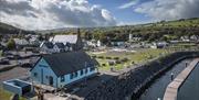 Aerial view of blue Glenarm Tourism building with town in the background and marina jetty in the foreground