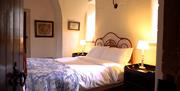 Door opening into the bedroom. Cosy double bed with a red iron bedframe. There is a side table on either side with lamps.