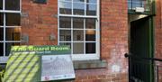 Entrance to The Guard Room with red brick building, and information panel in front of windows