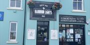 Black and white exterior sign for Harbour Lights Cafe on blue building with Carnlough Community Association building beside it.