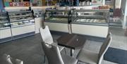 Grey seats and table with ice cream counters and food display fridges in the background