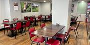 Dark wood tables with red trimmed chairs, wooden floors and cow pictures on wall in Morelli's @ Mandy's Cafe