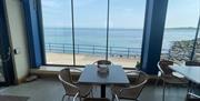 Table and seats within Prom Cafe looking out window to sea.