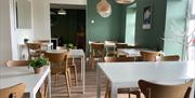 Interior of Quarter House Coffee Hoouse with white tables, wooden seats and sage green walls.