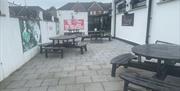 Outdoor seating area at Rubys Bar in Larne with black picnic tables, grey tiles and posters displaying support for Larne Football Club