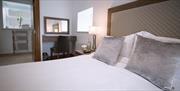 Bedroom with white sheets on bed and grey cushions and accessories