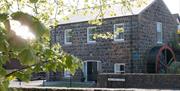 Stone Flax Mill restored self catering - black stone building with water wheel at side of house