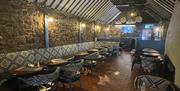 Back lounge bar of the Thatch Inn with wooden tables and fabric covered seats plus ceiling lit up with lights and TV on wall at far end of room