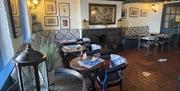 Front bar of The Thatch Inn with wooden seats and tables plus old pictures on the wall