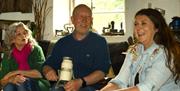 3 people chatting and laughing in the cottage while churning butter