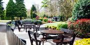 Outdoor seating area with dark wooden tables and seats surrounded by shrubs and garden