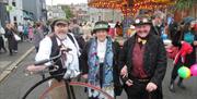 A photo of two men and a lady dressed in Victorian clothes standing with a penny farthing.