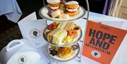 3 tier afternoon tea stand set up with sandwiches, scones and pastries plus Hope and Honour brochure