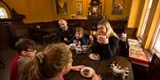 Family of 3 children and 2 adults sitting eating and drinking tea around a wooden dining table in the railway musuem cafe