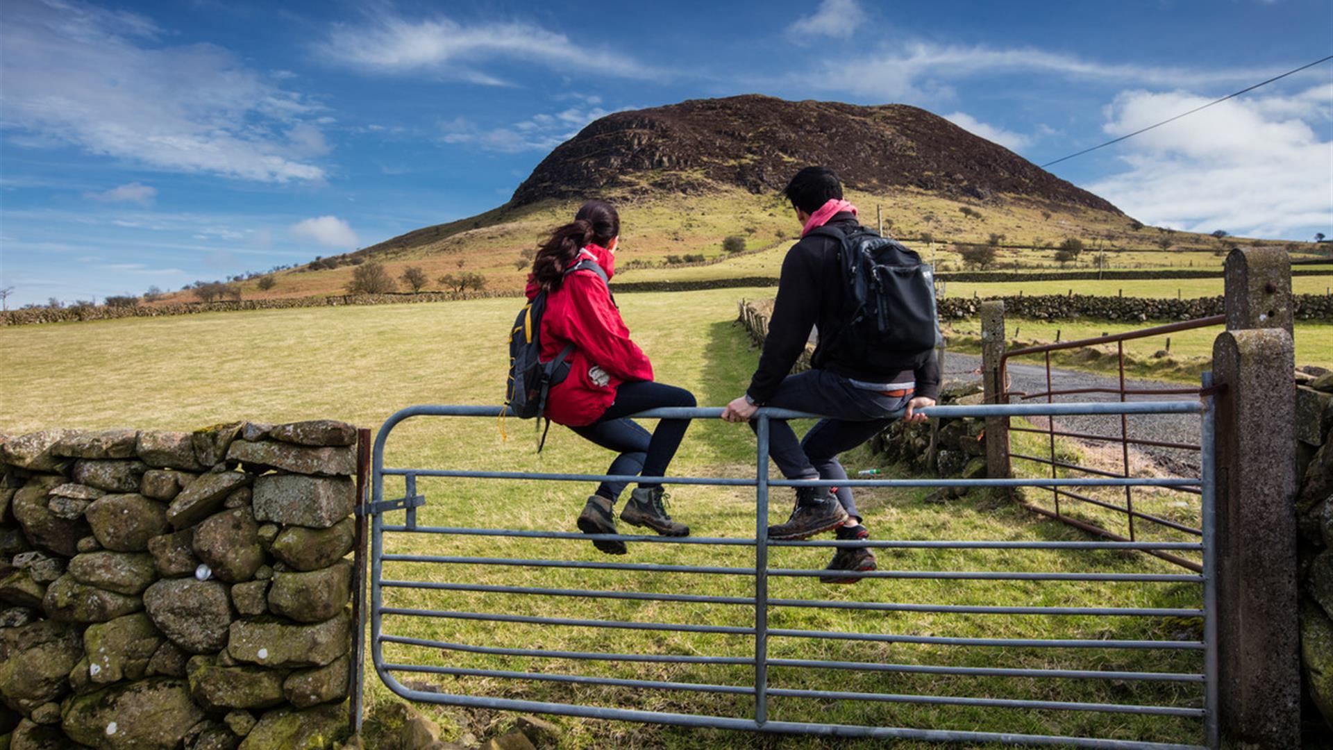 A couple of hikers sitting on a gate admiring the view of Slemish in the background