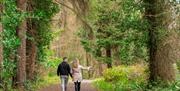 Man and woman walking along gravel path in Glenarm Forest surrounded by trees