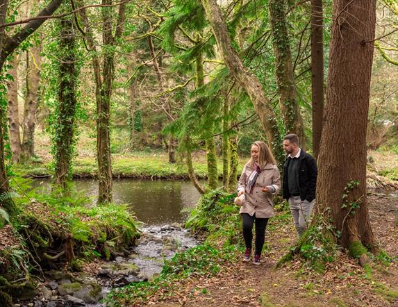 Man and woman walking alongside River in Glenarm Forest surrounded by trees