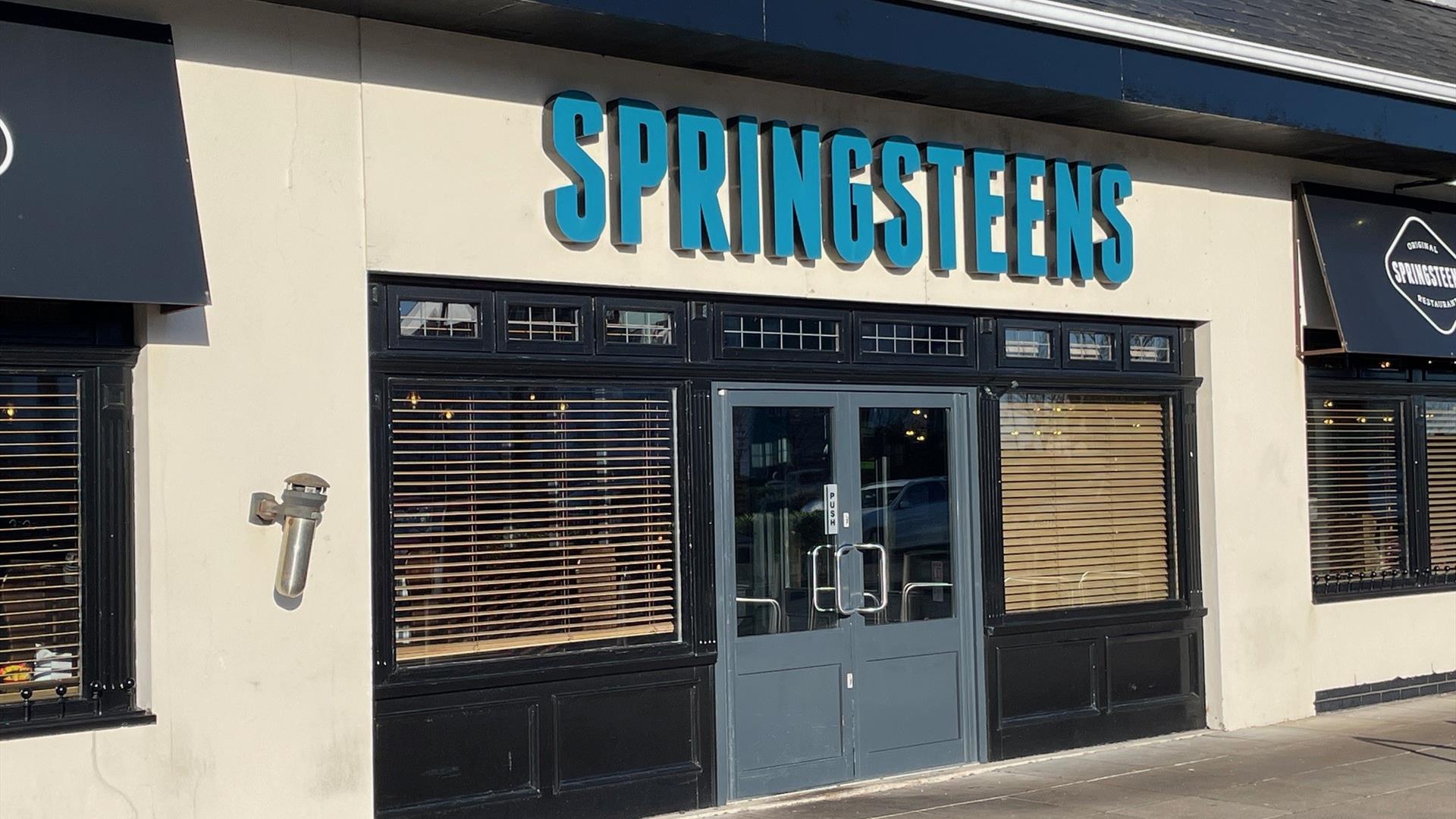 Exterior of Springsteens restaurant with grey doors and large sign.