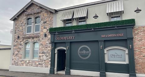 Entrance to the Olderfleet Bar with grey panel decoration, rustic brick walls and signage