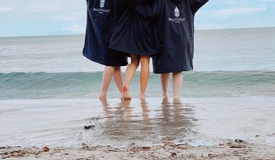 Group of friends on the beach in dry robes looking out to sea