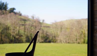 View of a field and trees from the sauna window with a bucket and ladle on the sauna bench