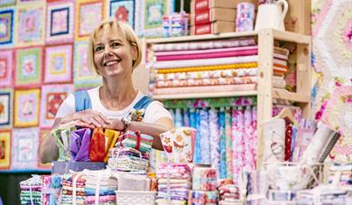 A craft stallholder stands smiling amongst craft supplies.