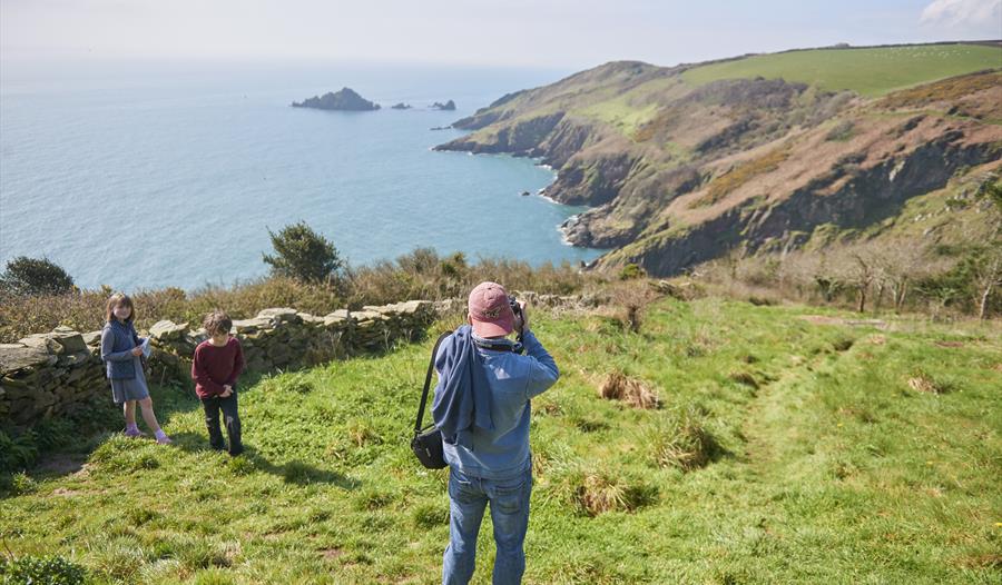 A photographer poised to take a photo of the rolling hills leading down to the sea at Coleton Fishacre.