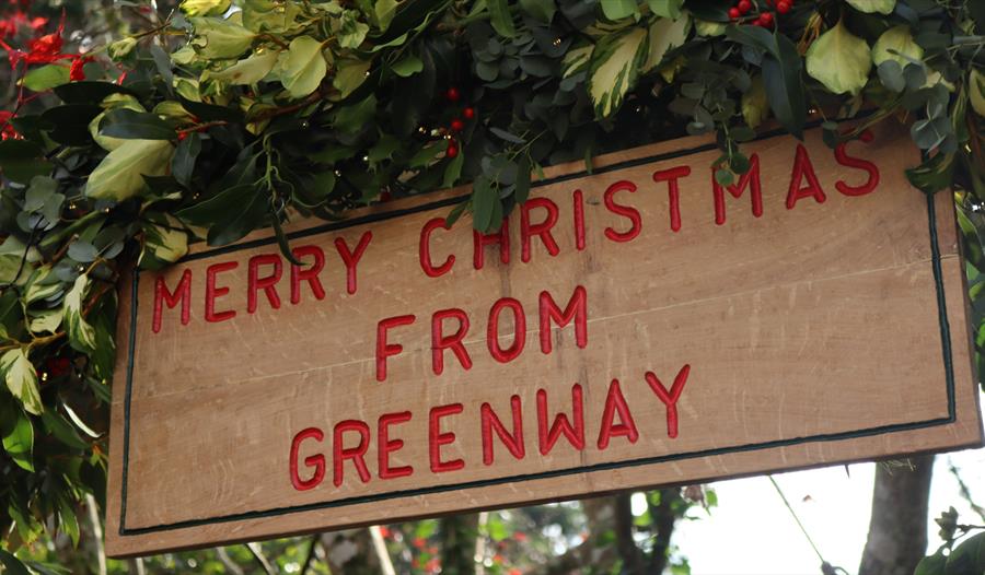 Wooden sign saying 'Merry Christmas from Greenway' with green foliage