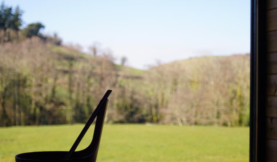View of a field and trees from the sauna window with a bucket and ladle on the sauna bench