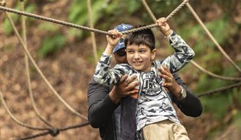 A child smiling and having fun playing on ropes guided by their parent.