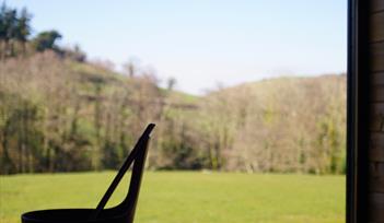 View of a field and trees from the sauna window with a bucket and ladle on the sauna bench
