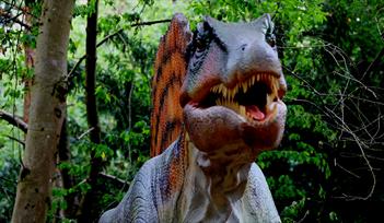 A scaley dinosaur with rows of sharp teeth and a colourful spine opens its jaws towards the viewer