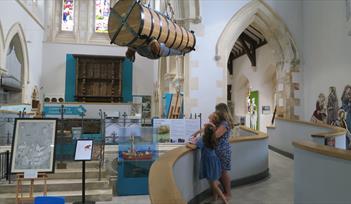 Photograph showing the main museum space with one adult and two children stood on a ramp looking up at the replica John Lethbridge Diving Engine
