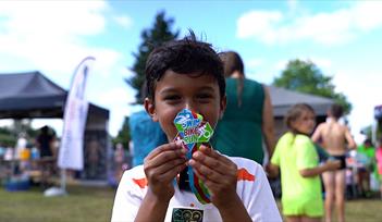 Young boy holding up swim bike run medal in front of face, smiling