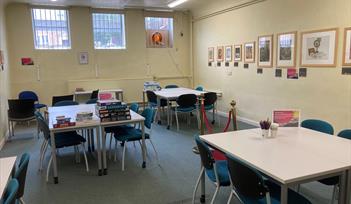 Tables and chairs with games and jigsaws on them are set out in a room.