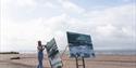 woman on the beach with two huge paintings of seascapes - Devon Open Studios