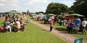 Groups of people sitting at picnic benches on the grass near the Grand Western Canal