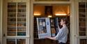 woman holding large painting of another woman standing outside a shop - Devon Open Studios