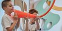 A boy speaks into a long orange speaking tube suspended from the ceiling